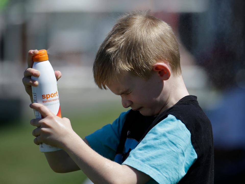 A boy sprays sunscreen on his face.