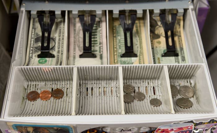 The cash register drawer is open, containing bills and coins in their assigned compartments