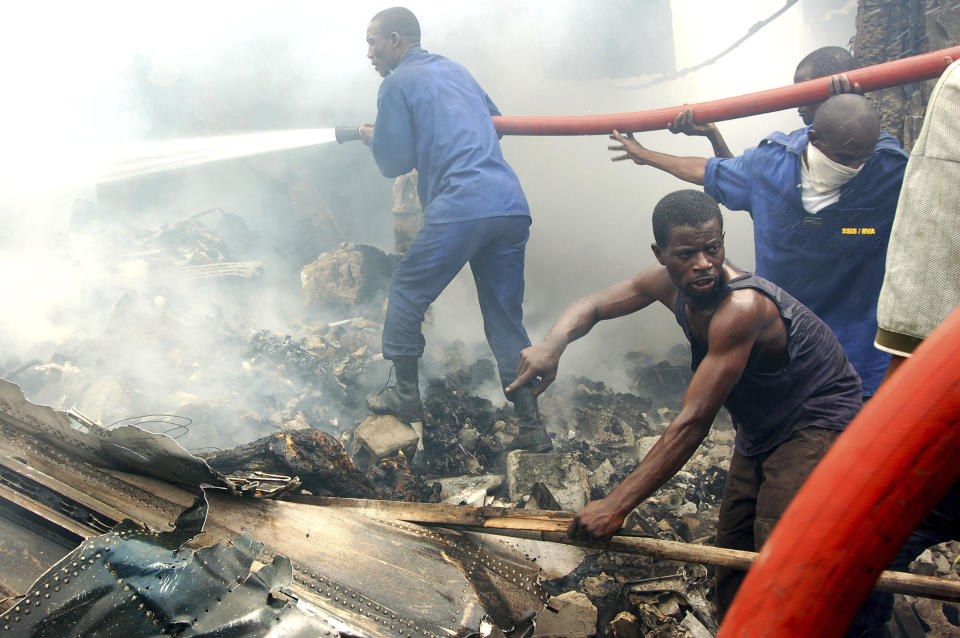 FILE - In this Oct 4 2007 file photo shot by AP contributing photographer John Bompengo, a rescue worker points out a charred body lying alongside a piece of a crashed cargo plane, as firefighters hose down the smoking rubble of a building, in Kinshasa, Democratic Republic of Congo. Relatives say longtime Associated Press contributor John Bompengo has died of COVID-19 in Congo's capital. Bompengo, who had covered his country's political turmoil over the course of 16 years, died Saturday, June 20, 2020 at a Kinshasa hospital. (AP Photo/John Bompengo, file)