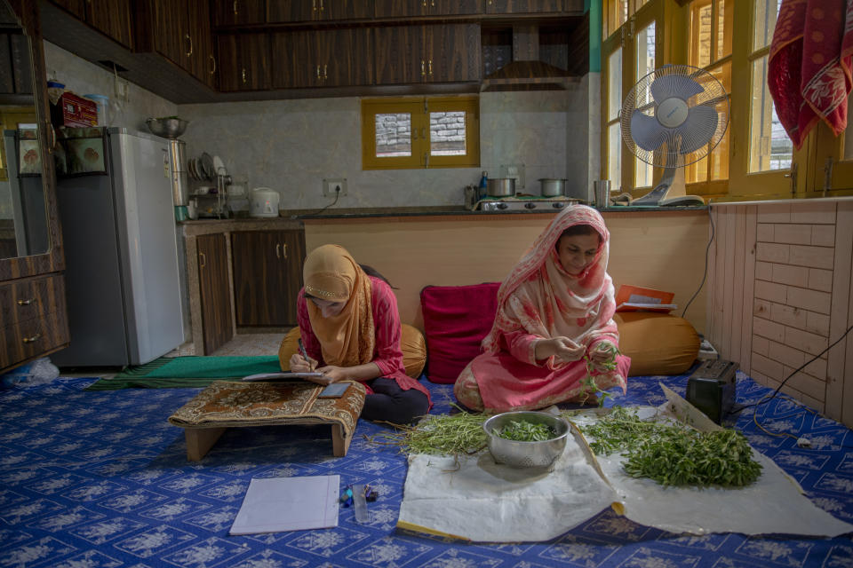 Kashmiri student Aaishya Imtiyaz writes her examination as her mother Nusrat Fatima cleans vegetables inside their kitchen in Srinagar, Indian controlled Kashmir, Wednesday, July 22, 2020. Experts say lack of formal schooling during the lockdown could have a serious psychological and emotional impact on the children. With no opportunity to be with friends, many homebound students are struggling to reimagine the school experience as parents take over the role of teachers. "This is my second exam at home since last year. I hope and pray that we go to school very soon," Aaishya said. (AP Photo/Dar Yasin)