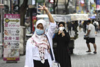 A woman wearing a face mask to help protect against the spread of the coronavirus takes photos of her friend at a shopping street in Seoul, South Korea, Wednesday, Aug. 5, 2020. (AP Photo/Ahn Young-joon)