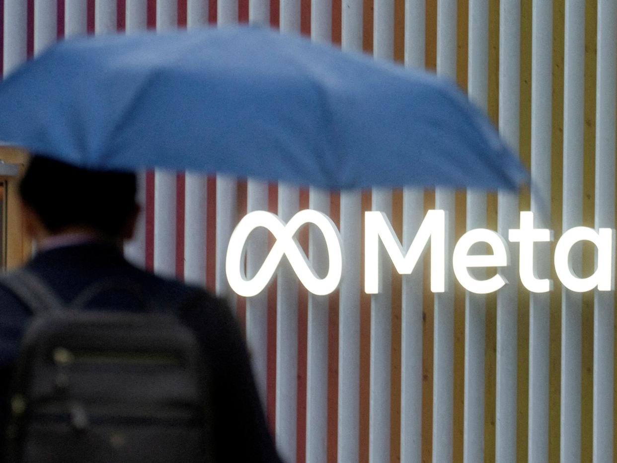 Man with blue umbrella with back against Meta logo.