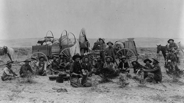 Cowboys sitting by supply wagons