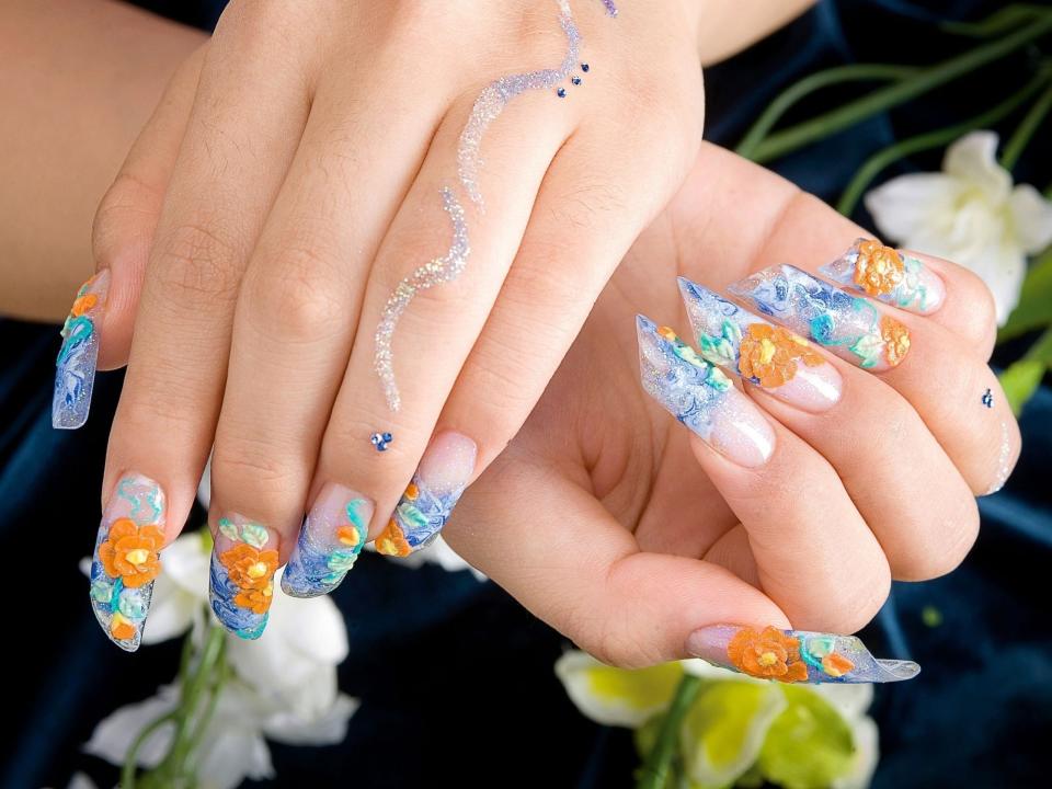 The image shows a pair of hands with painted nails. The nails are painted with nail polish and floral stickers