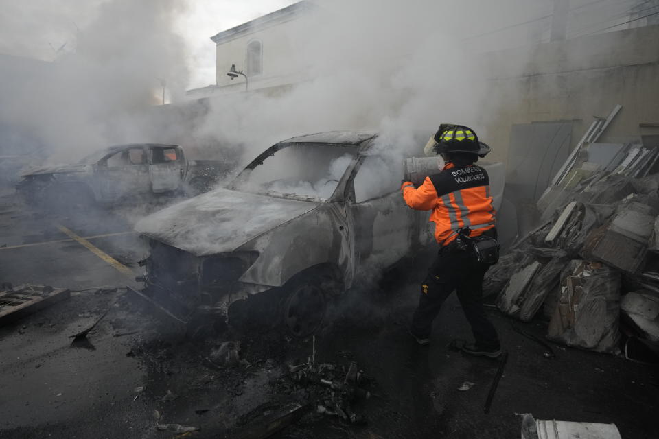 A firefighter douses a vehicle set on fire by a group of veterans demanding that a law be passed that compensates them for having served during the country's civil war, outside the Congress building in Guatemala City, Tuesday, Oct. 19, 2021. (AP Photo/Moises Castillo)