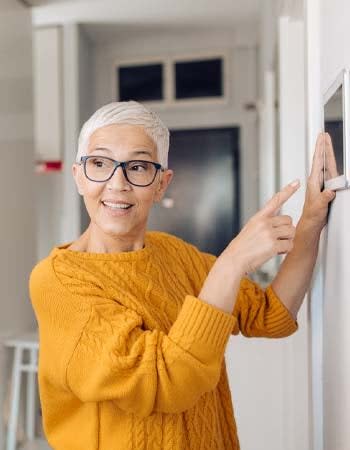 A woman points to a wall-mounted home security control panel.