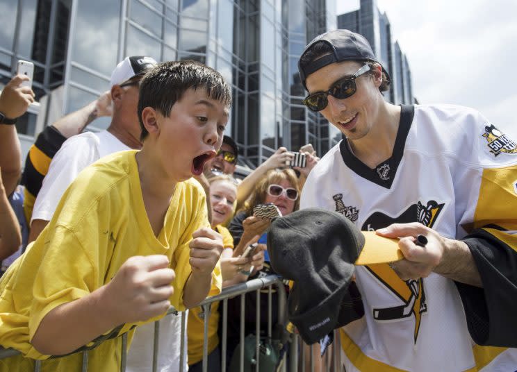 Pittsburgh Penguins’ Marc-Andre Fleury signs a hat for a young fan during the team’s Stanley Cup NHL hockey victory parade on Wednesday, June 14, 2017, in Pittsburgh.(Steph Chambers/Pittsburgh Post-Gazette via AP)