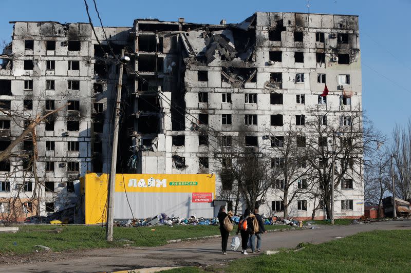 Local residents walk past a destroyed apartment building in Mariupol