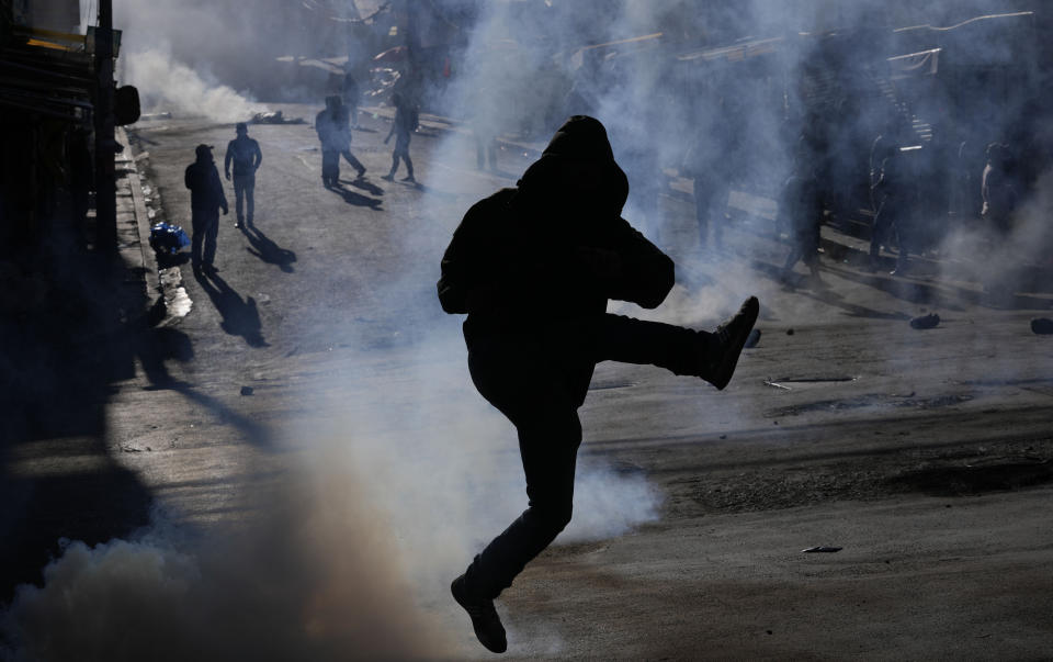 Un productor de hoja de coca patea una lata de gas lacrimógeno de vuelta a la policía en el tercer día de disturbios cerca de un mercado de coca en La Paz, Bolivia, el 3 de agosto de 2022. Agricultores contrarios al gobierno protestan contra un nuevo mercado paralelo de hoja de coca. (AP Foto/Juan Karita)