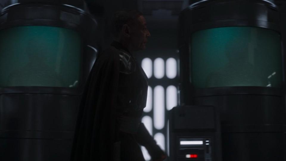 Moff gideon walks by two tanks of green liquid holding bodies on The Mandalorian