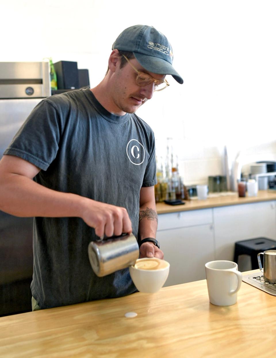 Owner Jesse Ingram uses foam to create latte art on a drink behind the counter at Comma. The shop serves traditional espresso-based drinks, drip coffee, tea and more with a focus on using seasonal ingredients.