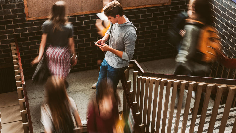 Young man standing on the staircase in college with girls walking by.