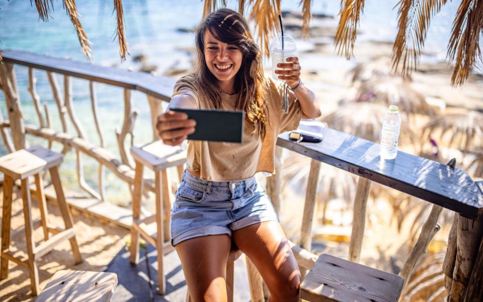 Photo of young smiling woman taking selfie at beach bar