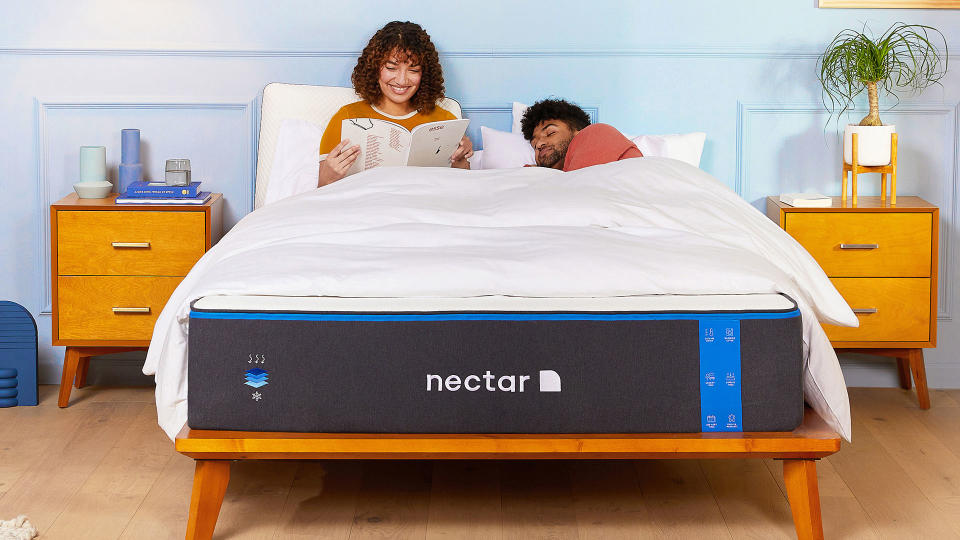 Nectar Memory Foam Mattress on a wooden bed base in a colourful room, with a couple sat up in bed