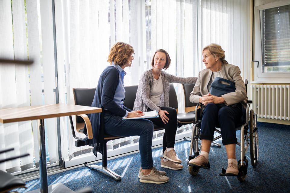 Three women in conversation, one seated in a wheelchair, in a brightly lit office room