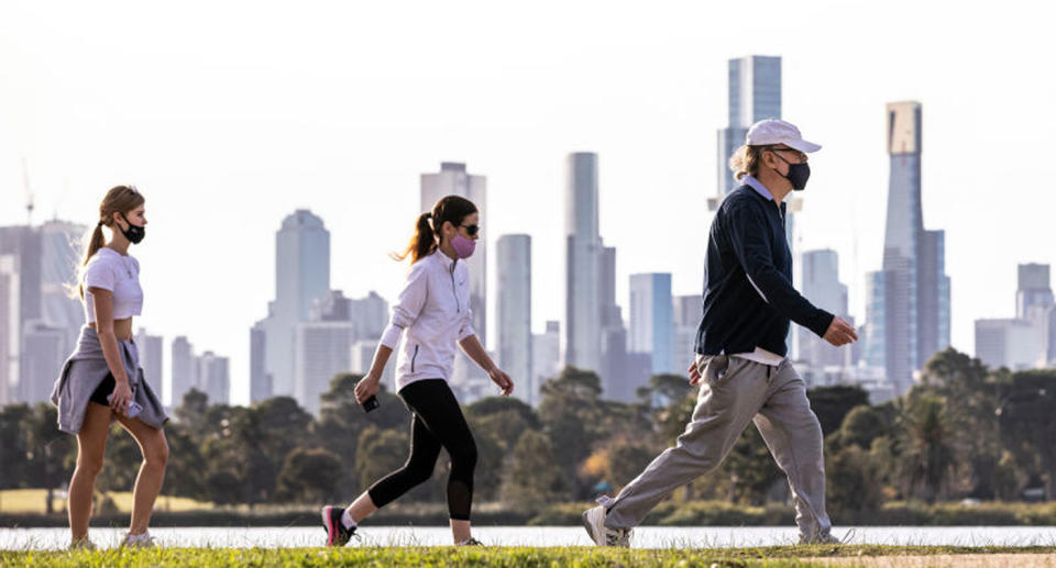 Three Victorians in mask walk along the Yarra River bank.