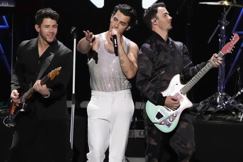 Three brothers perform onstage with instruments