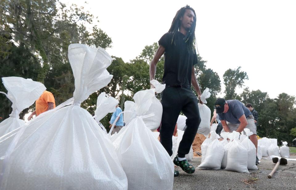 As Hurricane Ian sets its sights on Florida, a man carries sandbags to a waiting car on Monday as other residents fill more bags at a sandbag distribution site on Jean Street in Daytona Beach.