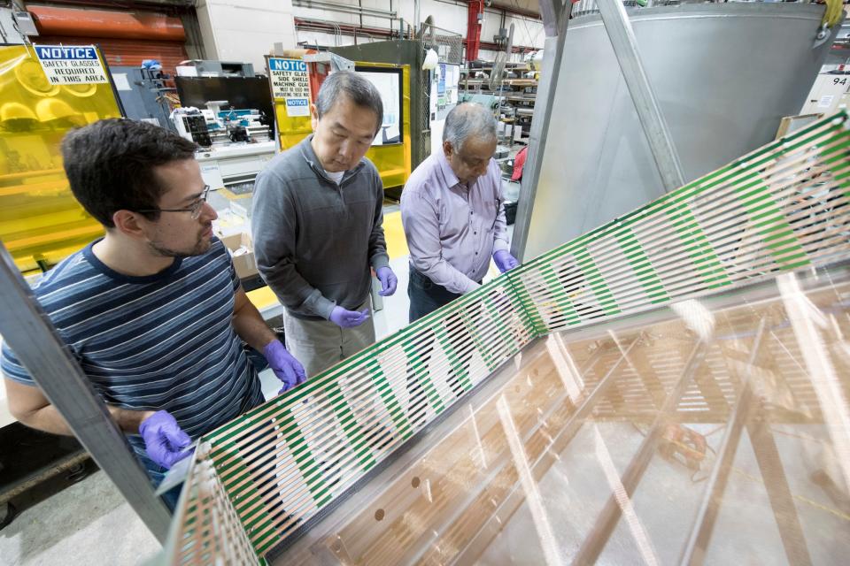 Three researchers look at a large reflective piece of electronic equipment that looks like a glass rectangle