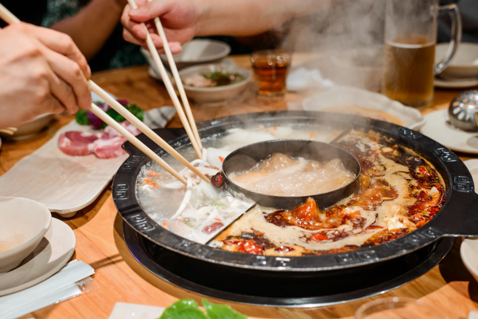 Eating a hot pot dish with chopsticks. Close up shot of appetizing food and traditional serving in Chinese restaurant.�