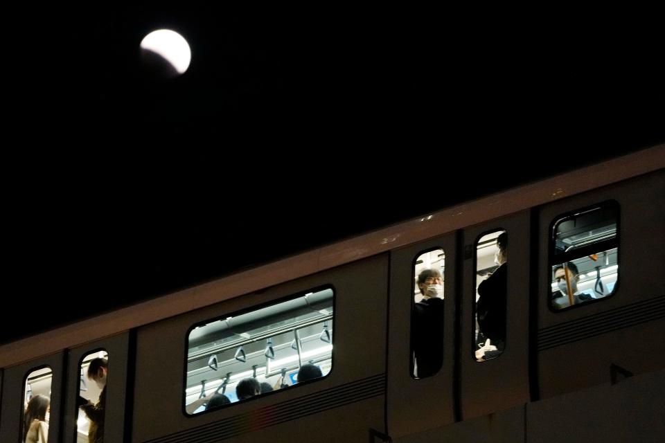 People ride on a train during a lunar eclipse over the Tokyo sky on Tuesday, Nov. 8, 2022.