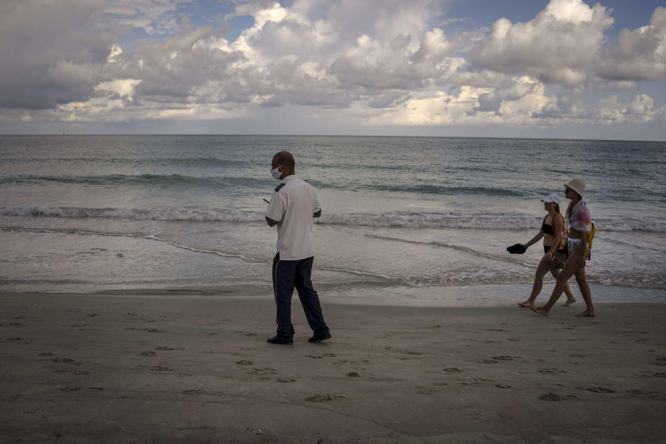 A security employee checks the beach while tourists walk on the beach of the Iberostar Selection Varadero hotel in Varadero, Cuba, Wednesday, Sept. 29, 2021. Authorities in Cuba have begun to relax COVID restrictions in several cities like Havana and Varadero. (AP Photo/Ramon Espinosa)