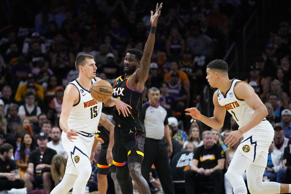 Denver Nuggets center Nikola Jokic (15) hands off to forward Michael Porter Jr. (1) as Phoenix Suns center Deandre Ayton (22) defends during the first half of Game 4 of an NBA basketball Western Conference semifinal game, Sunday, May 7, 2023, in Phoenix. (AP Photo/Matt York)