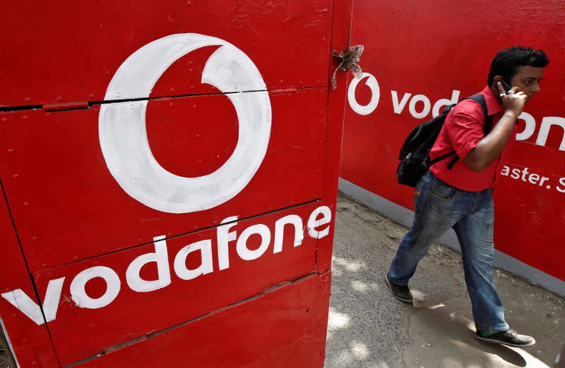 Man speaks on his mobile phone as he walks past the logos of Vodafone painted on a roadside wall in Kolkata