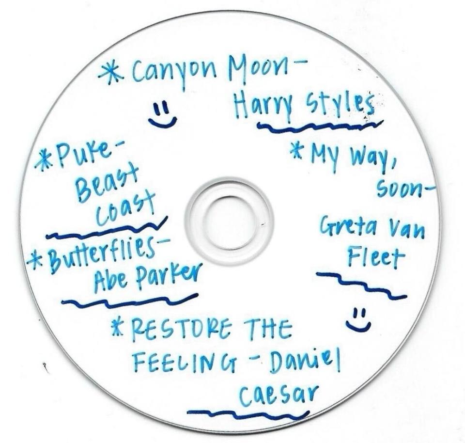 Handwritten tracklist on a white CD, including artists like Harry Styles and Daniel Caesar