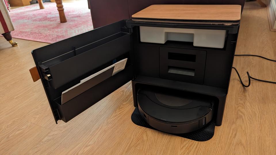 The Roomba Combo J9 Plus base with its door open, in front of a sofa