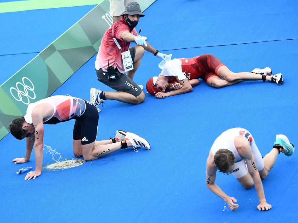 A triathlete pukes while others lay on the ground at the Tokyo Olympics.