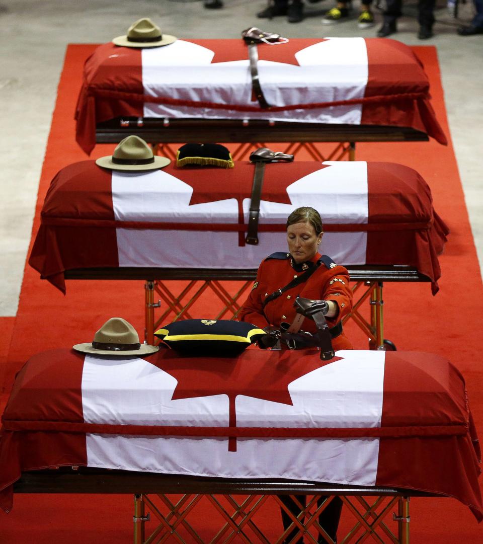 A Royal Canadian Mounted Police officer places a belt on one of three caskets during a regimental funeral for three fellow officers who were killed last week in Moncton