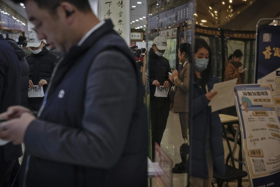 Chinese job seekers hold brochures is reflected on a mirror as they look for job vacancies at a job fair in Beijing on Feb. 23, 2024. China's efforts to restore confidence and rev up the economy will top the agenda during this month’s meeting of the ceremonial national legislature. (AP Photo/Andy Wong)