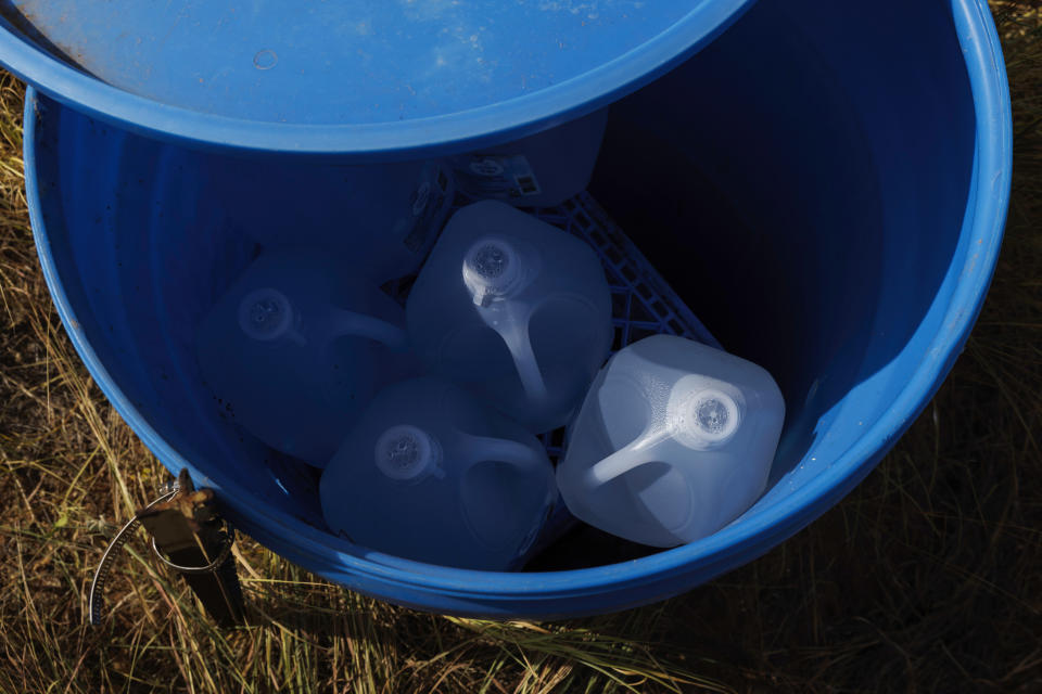 Sealed jugs of fresh water sit inside a water station for immigrants along a fence line near a roadway in rural Jim Hogg County, Texas, Tuesday, July 25, 2023. The South Texas Human Rights Center maintains over 100 blue barrels consistently stocked with water across rural South Texas to serve as a life-saving measure in the sweltering heat for immigrants who have crossed into the United States to travel north. (AP Photo/Michael Gonzalez)