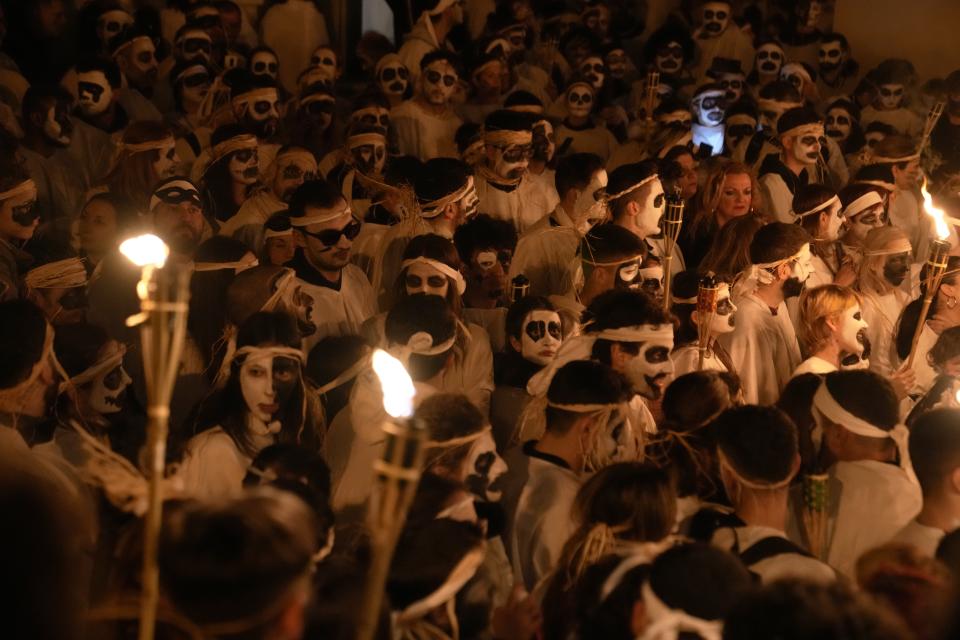 Young men and women with faces painted wear white sheets and hold torches on long poles, take part at the Torch Parade (Lampadiforia) on the Aegean Sea island of Naxos, Greece, late Saturday, Feb. 25, 2023. The first proper celebration of the Carnival after four years of COVID restrictions, has attracted throngs of revellers, Greek and foreign, with the young especially showing up in large numbers. (AP Photo/Thanassis Stavrakis)