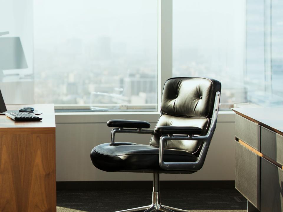 Bright corner office space with desk and empty leather chair