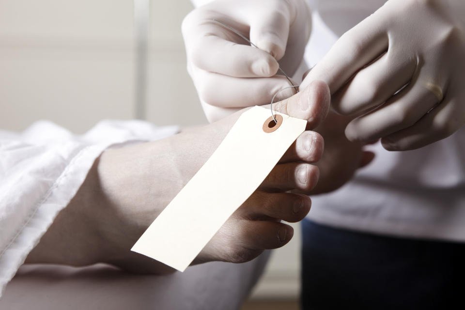 close up of gloved hands putting a tag on a body's toe