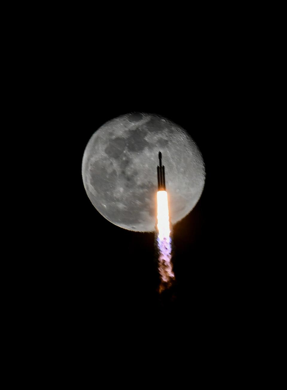 A SpaceX Falcon Heavy rocket flies across the face of the moon after its 8:07 p.m. liftoff from Kennedy Space Center.