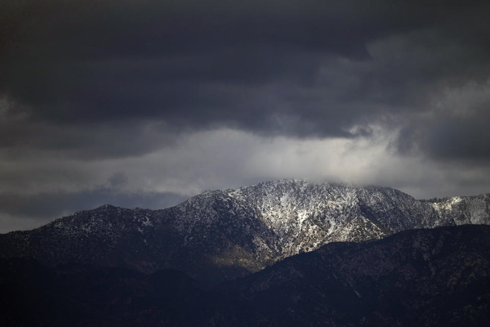 Heavy clouds move over the San Gabriel Mountains range in this view from Los Angeles, Thursday, Feb. 8, 2024. Snow-capped mountains sparkled under brilliant sunshine that replaced days of extreme wet weather that marked a major turnabout from a very slow start to winter. (AP Photo/Damian Dovarganes)