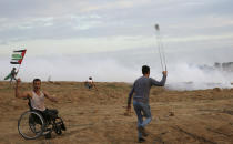 Protesters hurl stones at Israeli troops while fired teargas near the fence of Gaza Strip border with Israel during a protest east of Gaza City, Friday, Nov. 16, 2018. (AP Photo/Adel Hana)