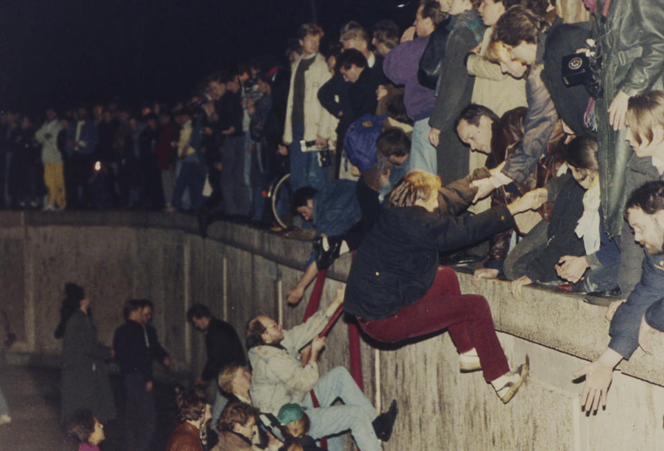FILE - East Berliners get helping hands from West Berliners as they climb the Berlin Wall which has divided the city since the end of World War II, near the Brandenburger Tor (Branderburg Gate), early Friday morning, Nov. 10, 1989. (AP Photo/Jockel Finck, File)