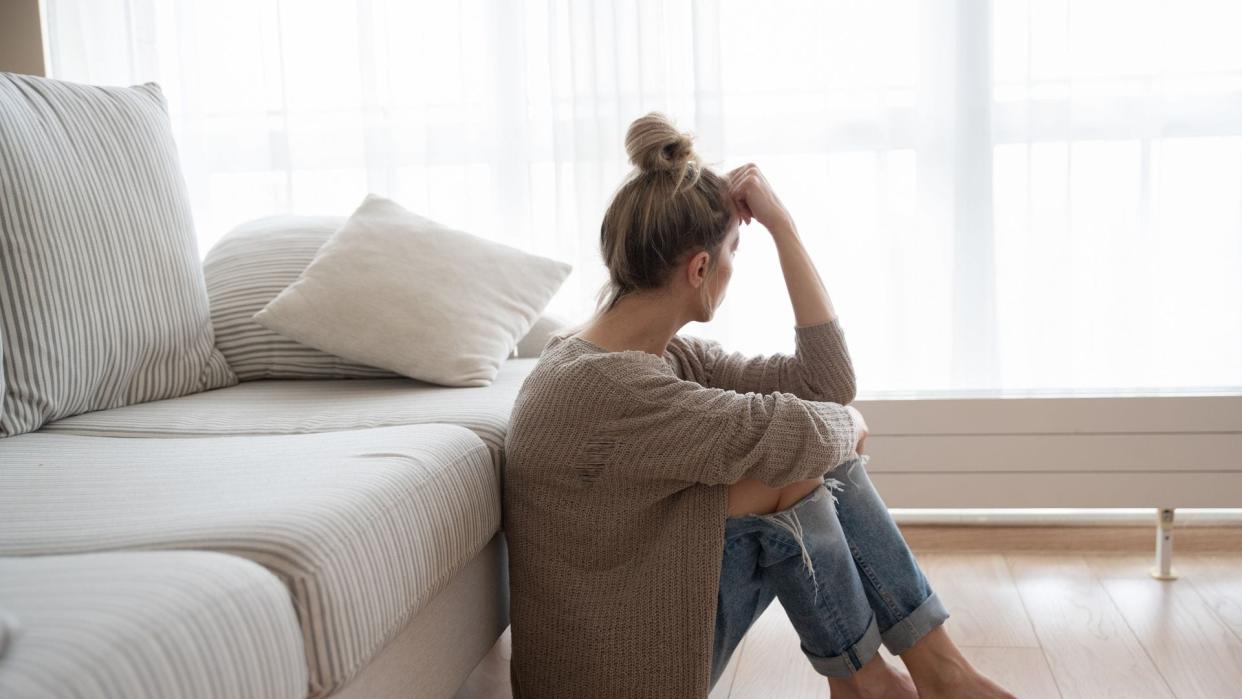 mujer cansada sentada en el suelo, junto al sofá