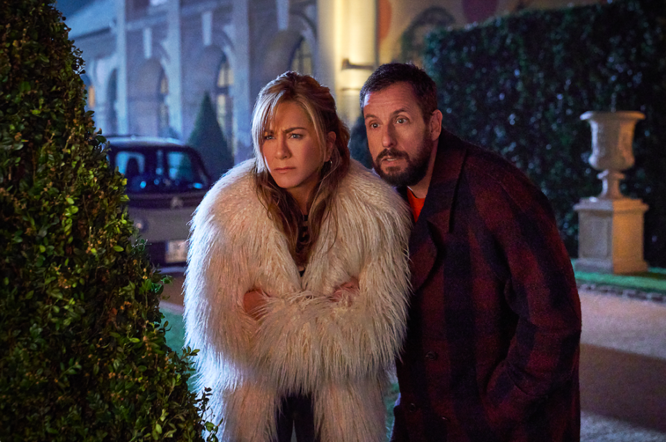 Jennifer Aniston and Adam Sandler peer from behind a hedge