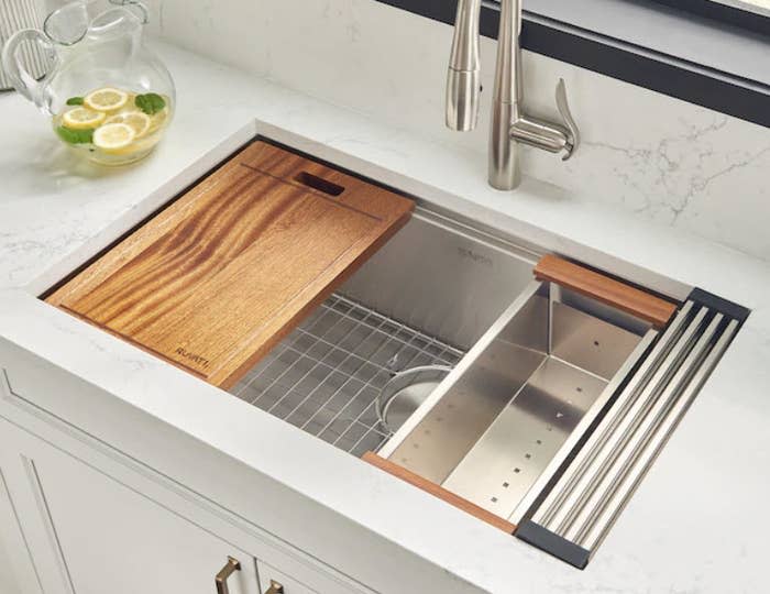 stainless steel farmhouse sink with wooden cutting board and drying rack