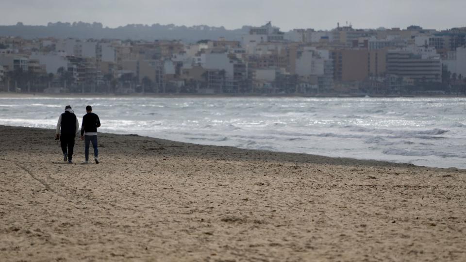 Zwei Männer gehen am Strand von Arenal über den Sand. (Bild: dpa)
