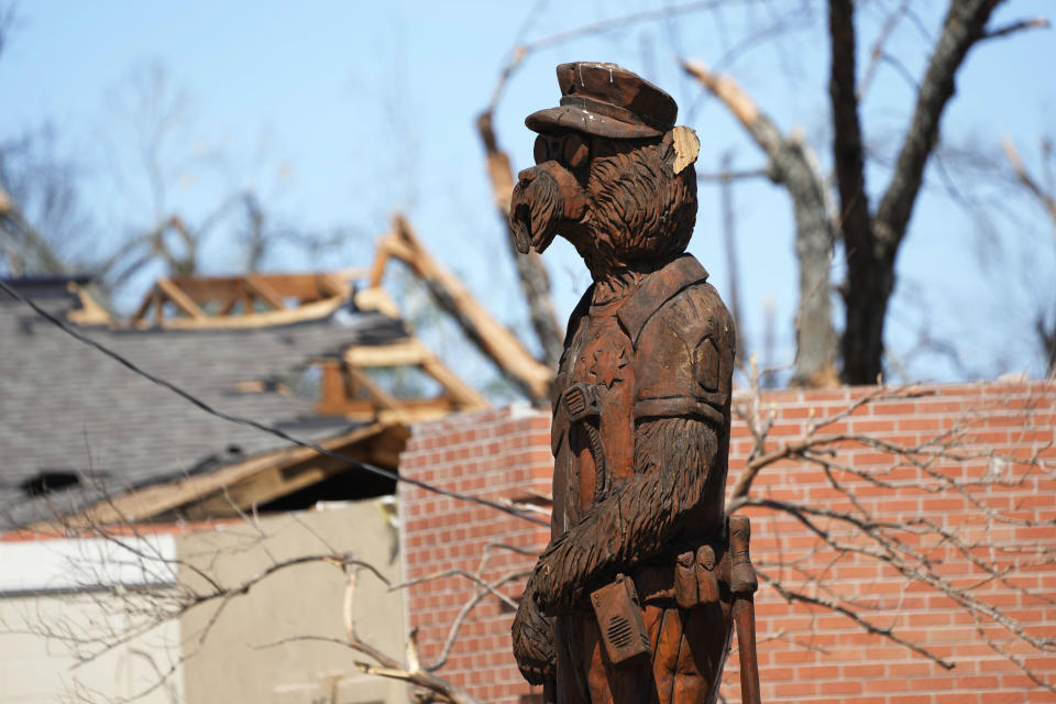 A damaged but upright 12-foot wood carved "officer bear" stands in front of the heavily damaged Rolling Fork, Miss., police station, a victim of the March 24 killer tornado that hit a number of Mississippi communities, on March 29, 2023. The statue is one of almost 20 spread throughout the city of 2,000 that commemorates the county legend of the day former President Theodore Roosevelt, nicknamed Teddy, refused to kill a captured bear on a hunting trip there, calling the act unsportsmanlike. (AP Photo/Rogelio V. Solis)