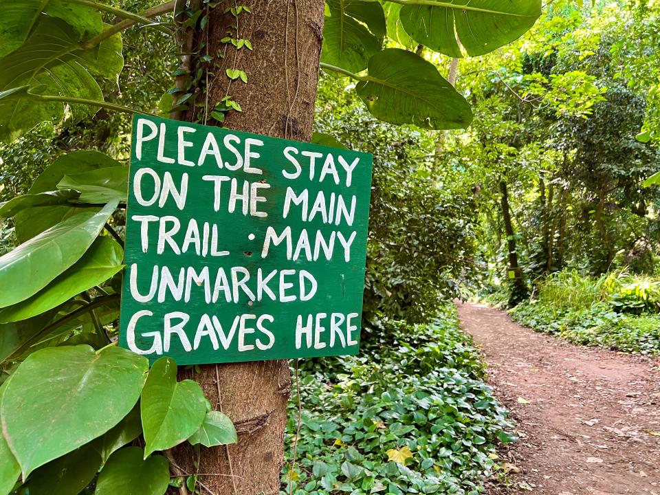 A sign in a Hawaii tree saying to stay on the main trail because there are unmarked graves