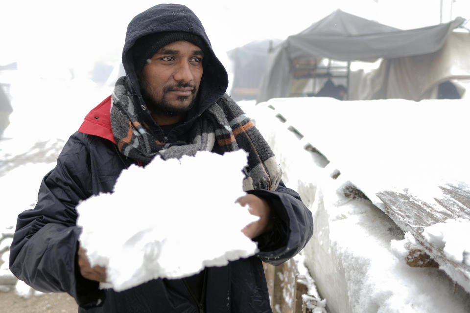 A migrant carries snow to isolate his makeshift shelter at the Lipa camp, outside Bihac, Bosnia, Friday, Jan. 8, 2021. A fresh spate of snowy and very cold winter weather on has brought more misery for hundreds of migrants who have been stuck for days in a burnt out camp in northwest Bosnia waiting for heating and other facilities. (AP Photo/Kemal Softic)