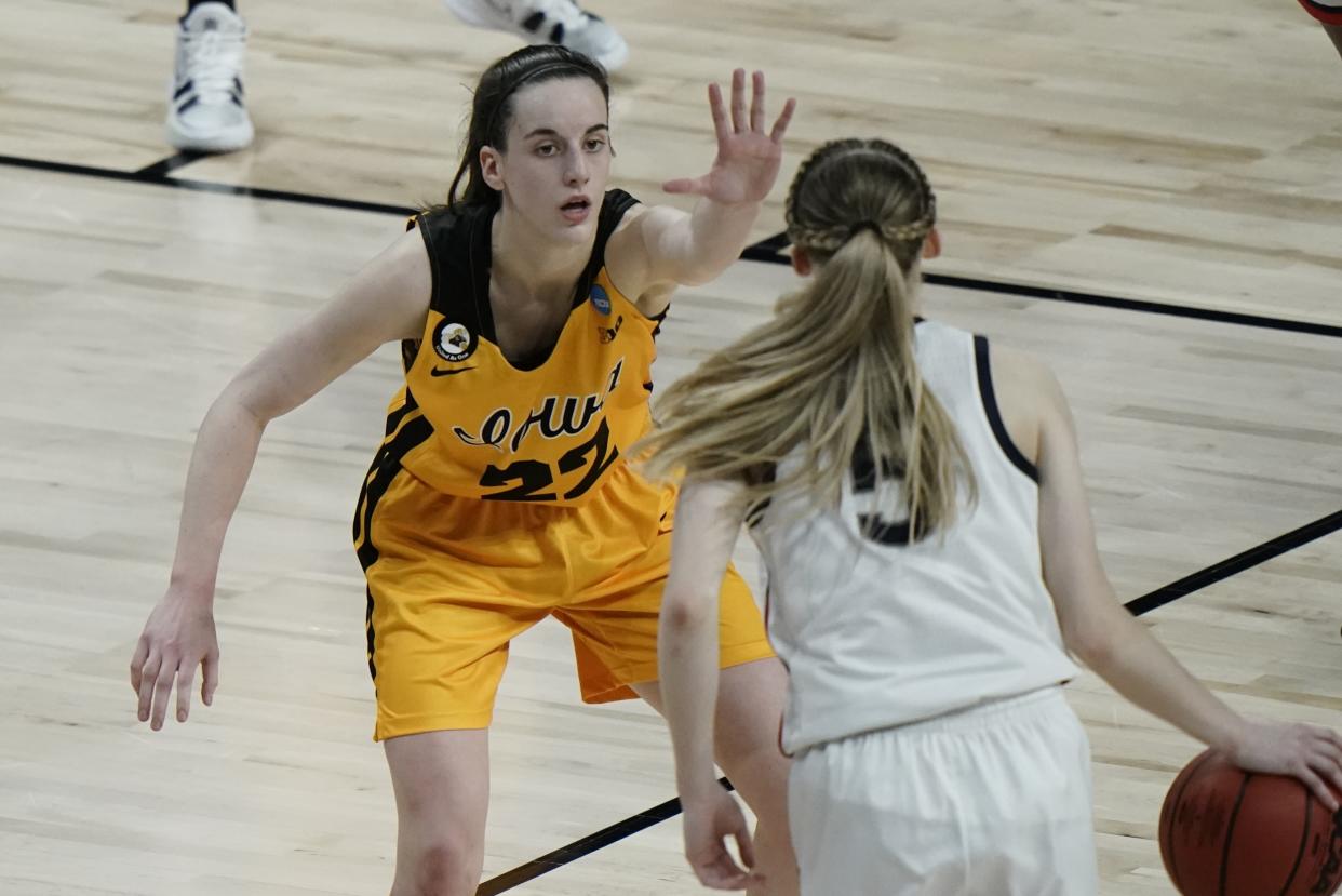 Caitlin Clark faces the camera with her hand up to defend Paige Bueckers who has her back to the camera with the ball in her hand.