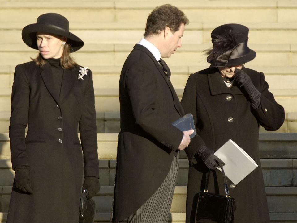 sarah chatto, viscount linley and queen elizabeth stand outside on a sunny day in black formal attire, the women wear hats and hold purses, the man holds a book and talks to elizabeth